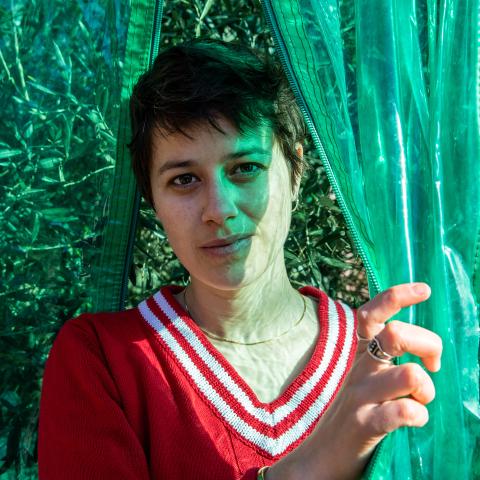 Sarah Elena Müller schaut hinter einem grünen Plastikvorhang hervor