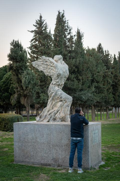 Mamo steht mit verdecktem Gesicht bei einer Statue