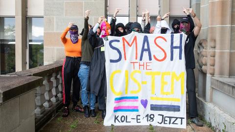 vermummte Student:innen vor dem Uni-Gebäude Zürich mit einem Transparent auf dem «SMASH THE CIS-TEM – KOL-E-18 JETZT» steht