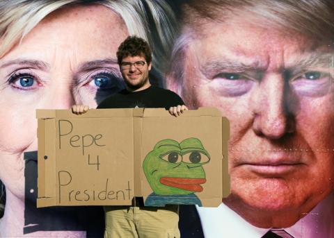 Ein Mann hält ein «Pepe the Frog»-Schild vor dem Konterfei von Hillary Clinton und Donald Trump hoch