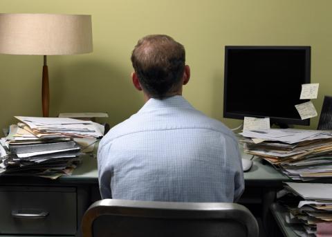 Symbolbild: Person in einem Büro mit vielen Aktenstapeln