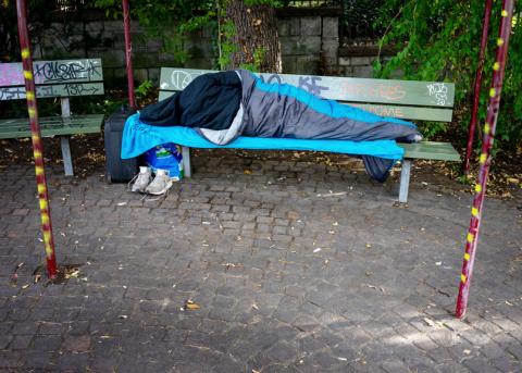Obdachloser, welcher auf einer Sitzbank schläft