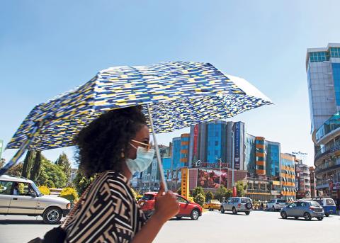 Frau mit Sonnenschirm an befahrener Strasse in Addis Abeba
