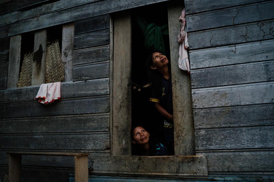 duas mulheres indígenas olham para fora da porta de uma cabana simples