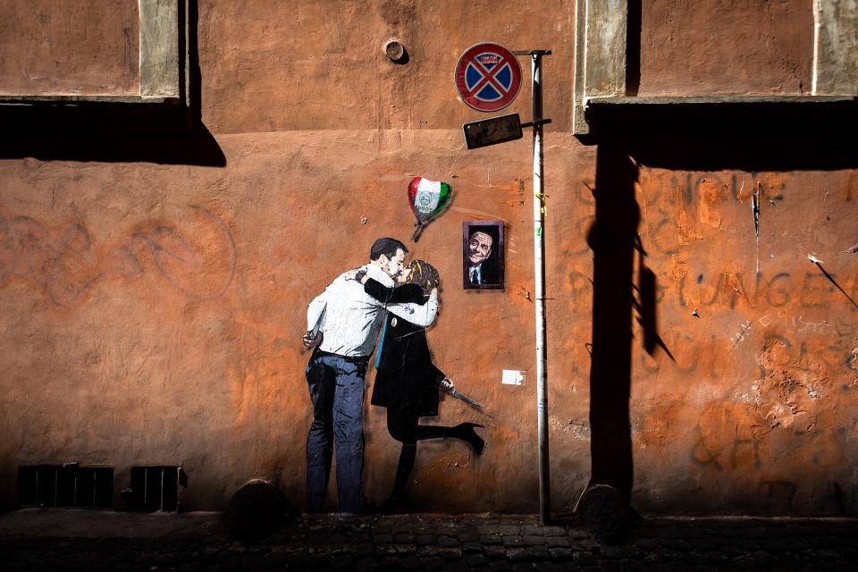 Stencil Graffiti an einer Hauswand: ein Paar küsst sich, daneben schaut Berlusconi aus einem Fenster