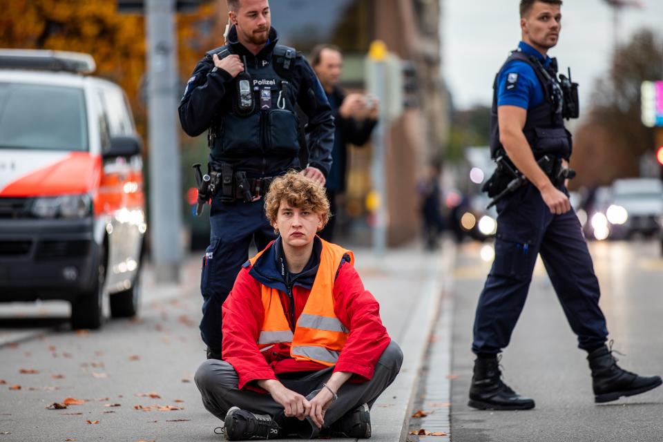 eine Person sitzt auf der Strasse, dahinter zwei Polizeibeamte