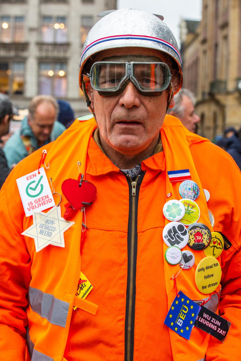 Demonstrant mit oranger Weste mit vielen Aufsteckern und silbrigem Helm
