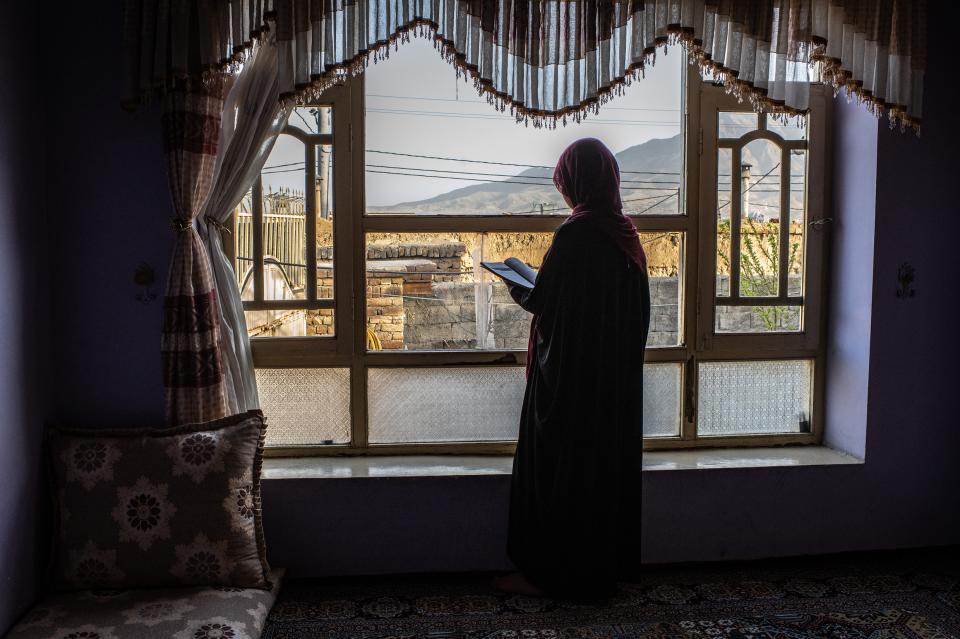 Junge Frau in Kabul, welche am Fenster steht und ein Buch anschaut