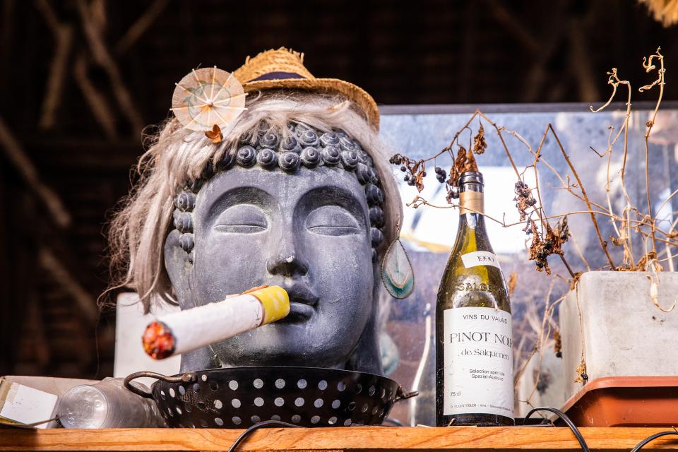 eine asiatische Skulptur als Kopf mit einer grossen Zigarette im Mund, daneben eine Weissweinflasche