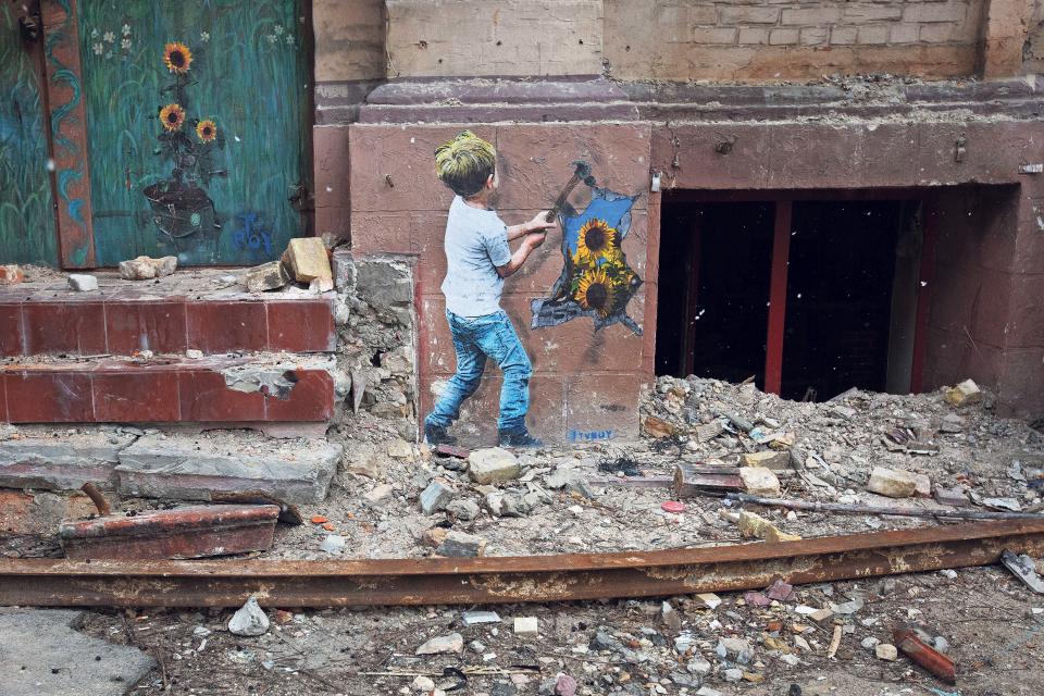 Graffiti an einer Hauswand: ein Junge schlägt mit einem Hammer ein Loch in die Wand, durch das Loch wachsen Sonnenblumen
