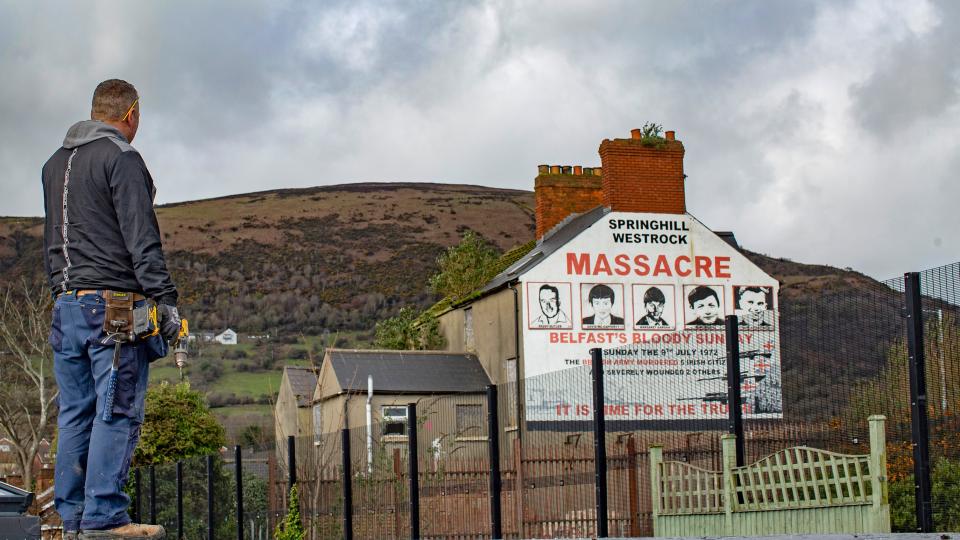 ein Mann in Arbeitskleidung schaut auf ein Wandgemälde im Belfaster Stadtteil Springhill