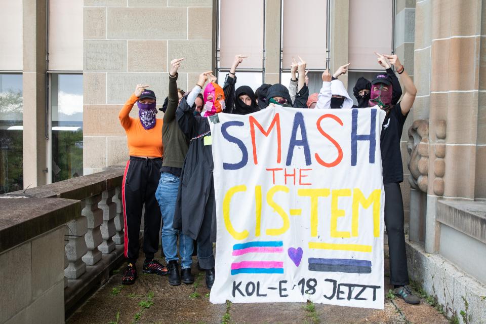 vermummte Student:innen vor dem Uni-Gebäude Zürich mit einem Transparent auf dem «SMASH THE CIS-TEM – KOL-E-18 JETZT» steht
