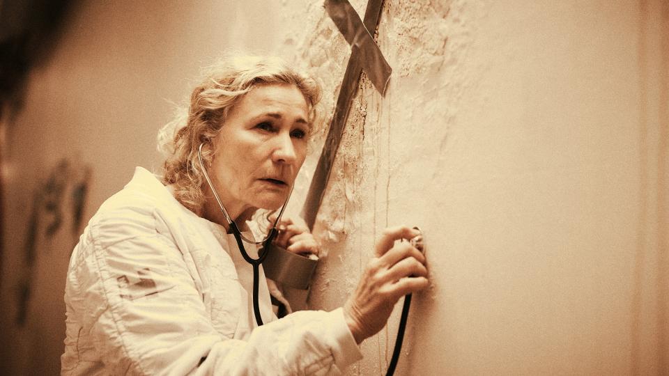 Still aus dem Film Geister: Exodus»: eine Frau hört mit dem Stethoskop eine Wand ab